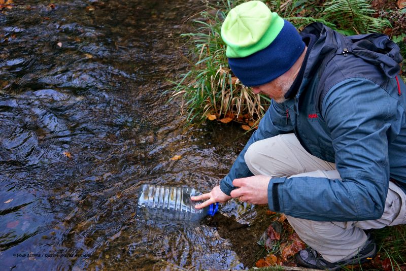 man-scooping-water-plastic-bottle-river