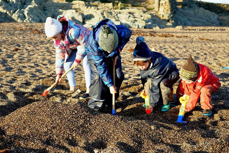 four-children-digging-beach-dark-sand-winter-sunlight