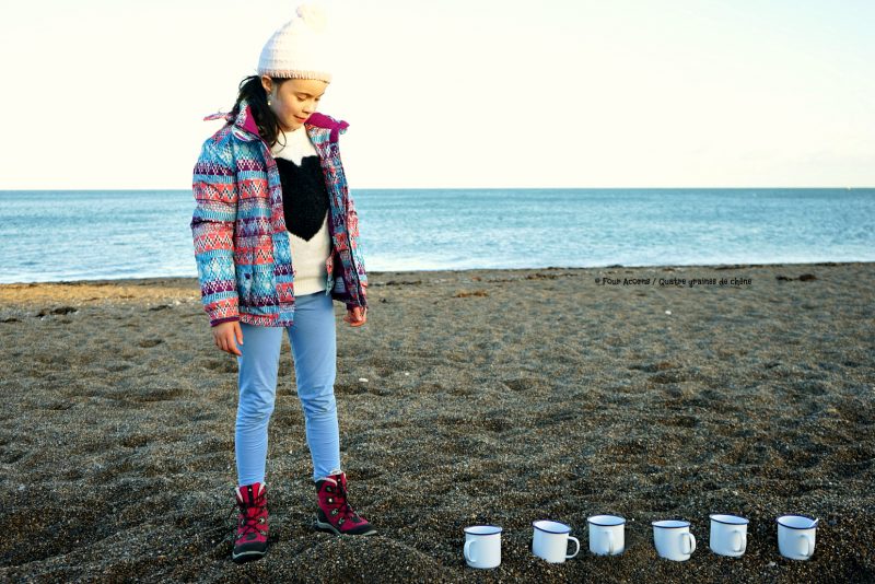 girl-standing-beach-beside-six-white-cups-sand