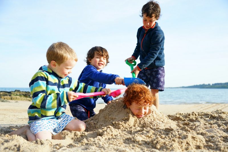 four-boys-playing-buried-sand-beach-wicklow-ireland