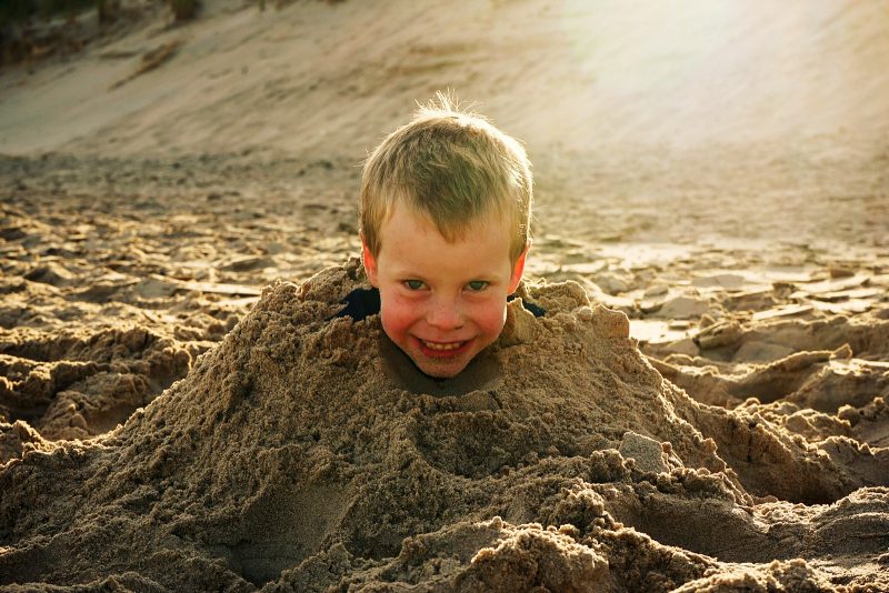 boy-head-buried-in-sand-beach-sunglow-wicklow-ireland