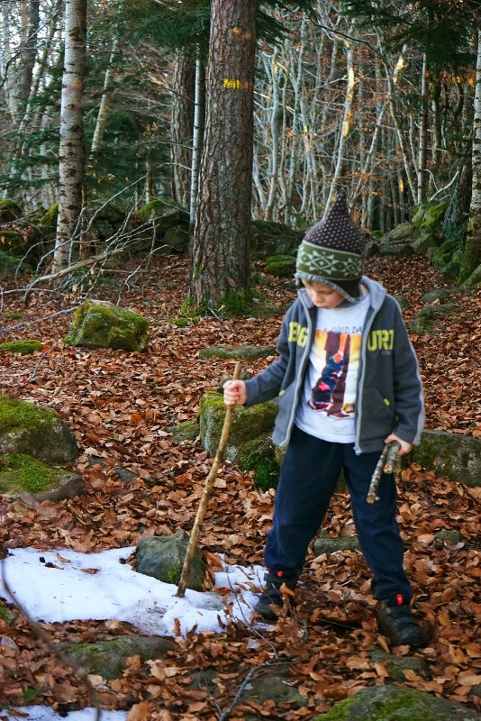 child-poking-snow-with-stick-elf-hat